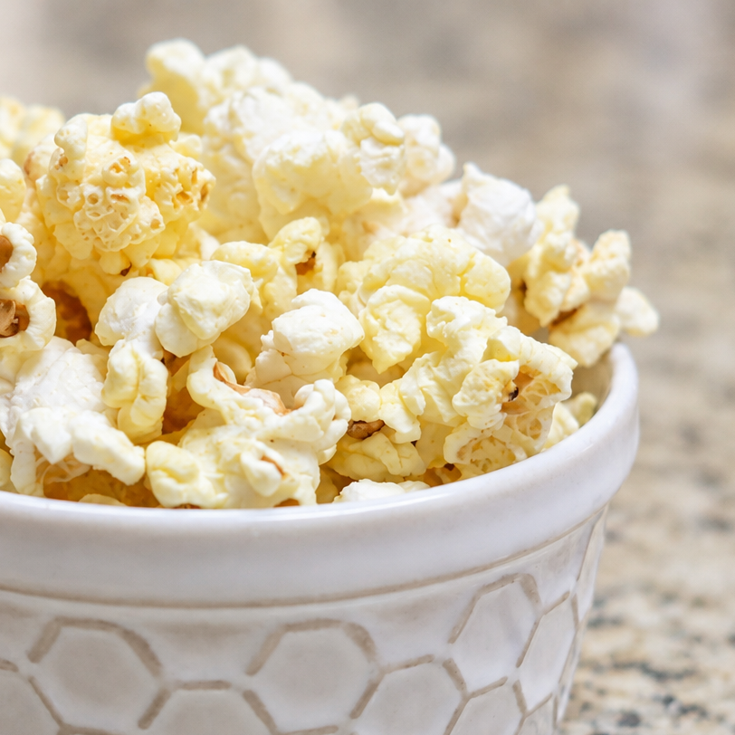 A white ceramic bowl with a honeycomb pattern, filled with fluffy popcorn, set on a speckled granite countertop.