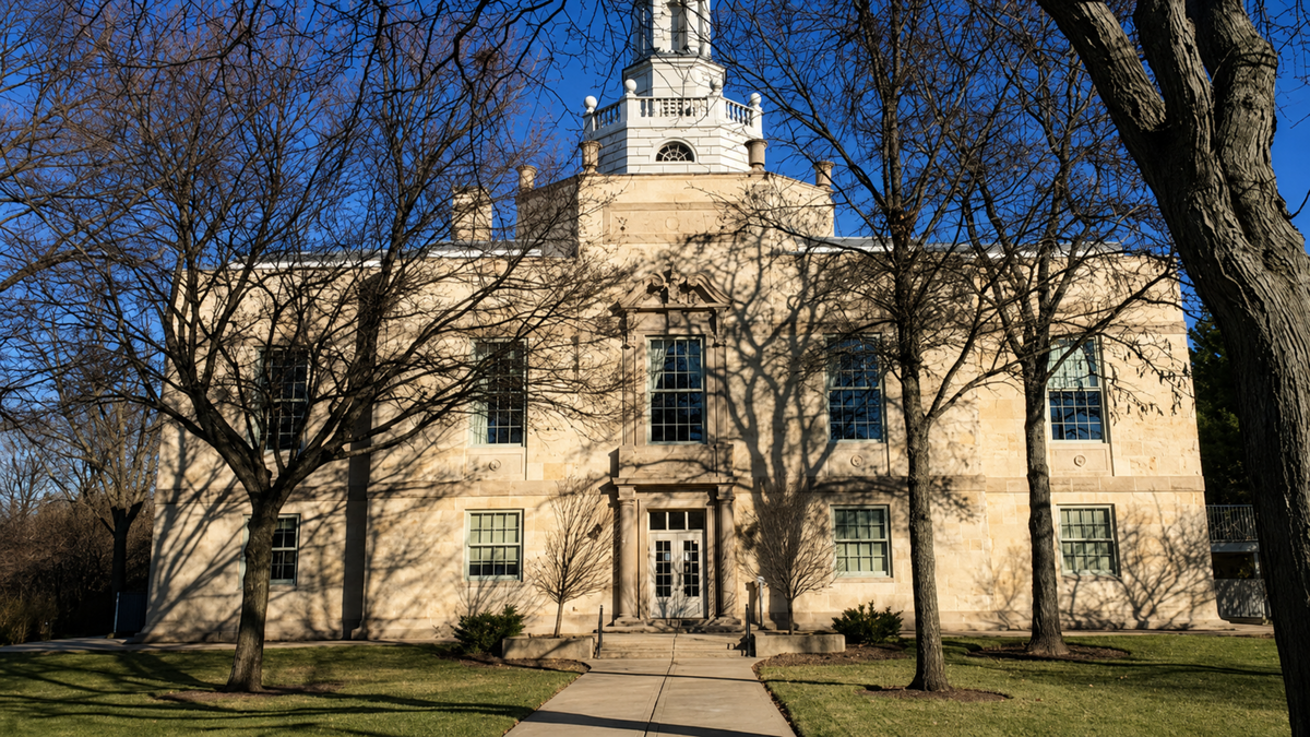 A large beige stone building in Highland Park, IL with a central tower and arched entryway, framed by leafless trees and a paved walkway under a clear blue sky.